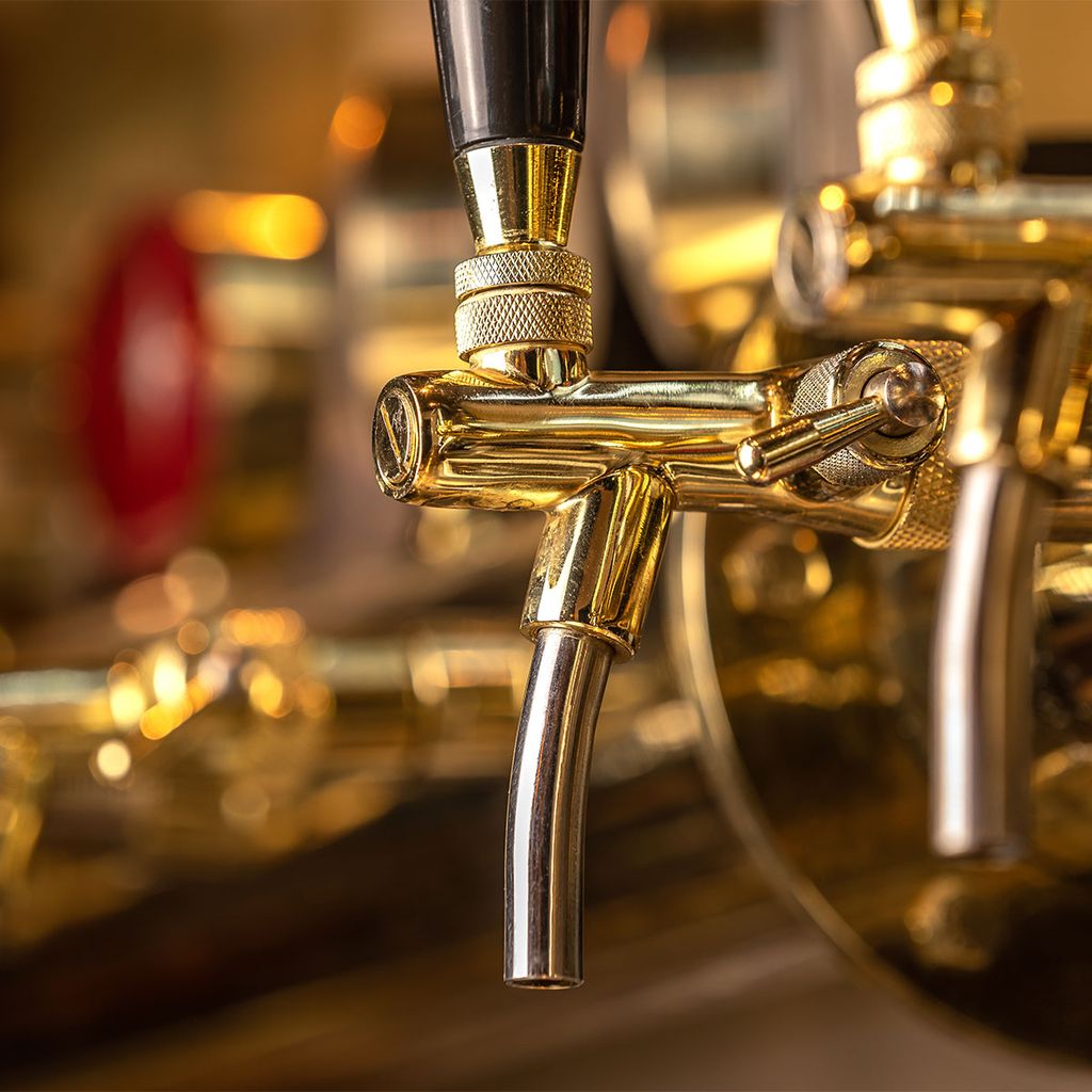 Nahaufnahme eines glänzenden, goldenen Bierhahns mit schwarzem Griff